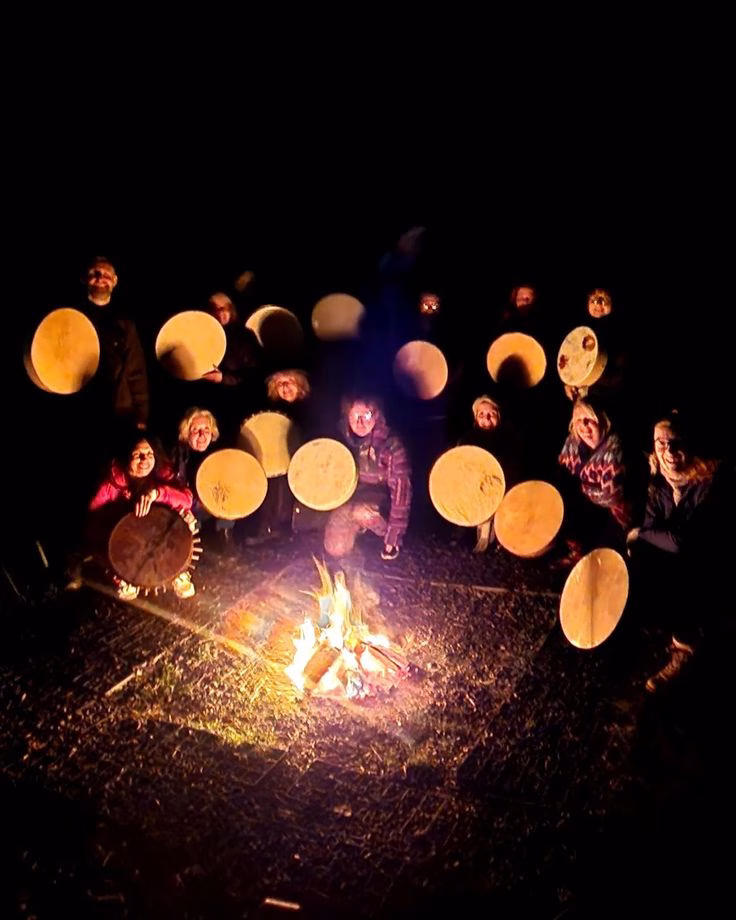 Group drumming in a Shamanic circle under dim lighting.